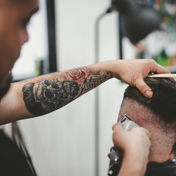 Friseur:in rasiert einer Person die Seiten